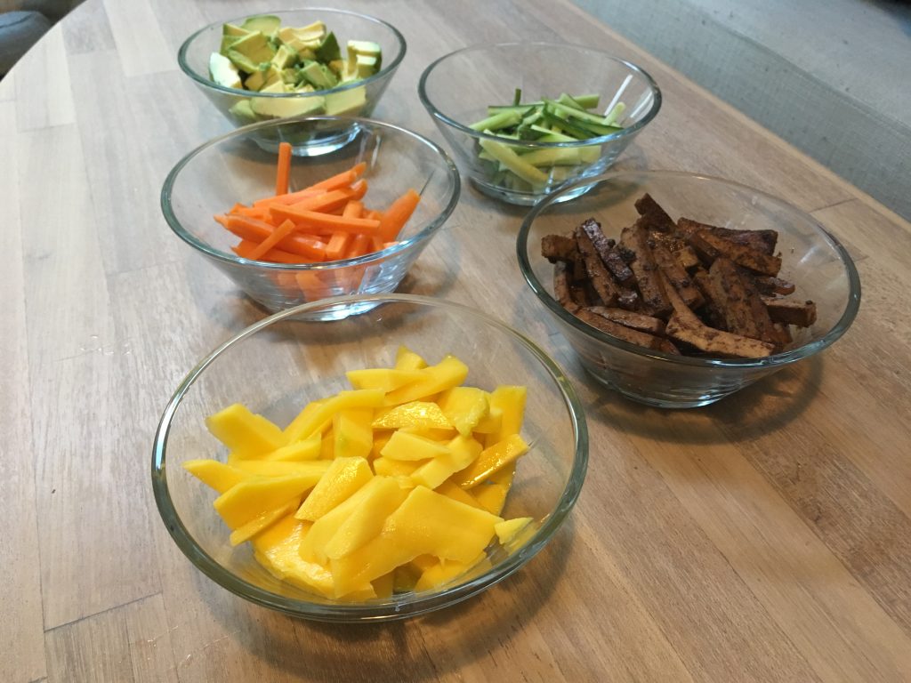 mango, tofu, gulerødder, avocado og agurk placeret i glasskåle på et træbord